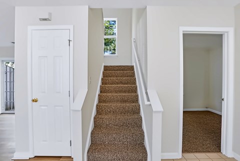 A staircase with a carpeted runner and white railings leads to a doorway.