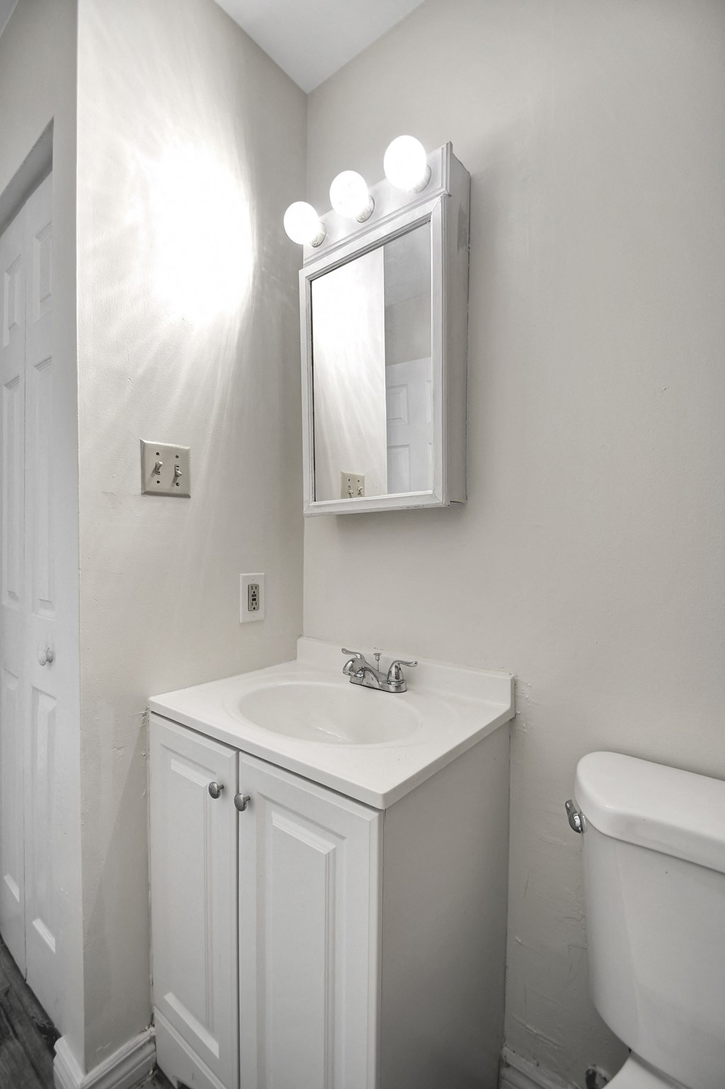 A white bathroom with a sink, mirror and toilet.