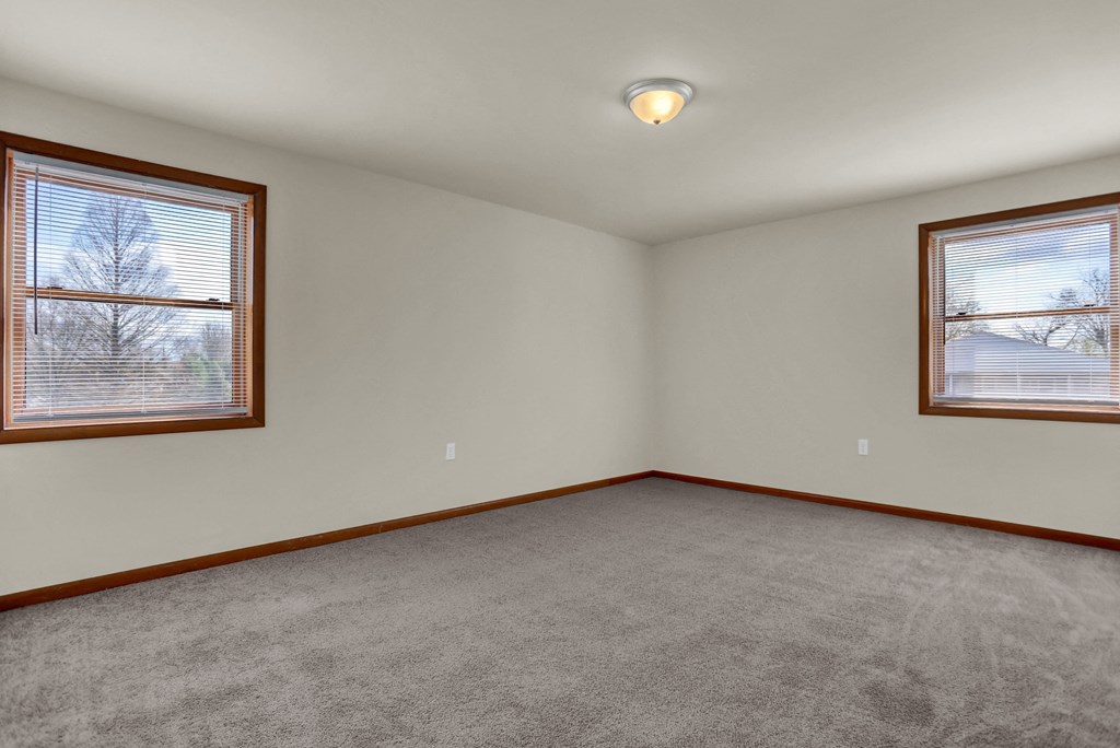 the living room of a house with carpet and two windows