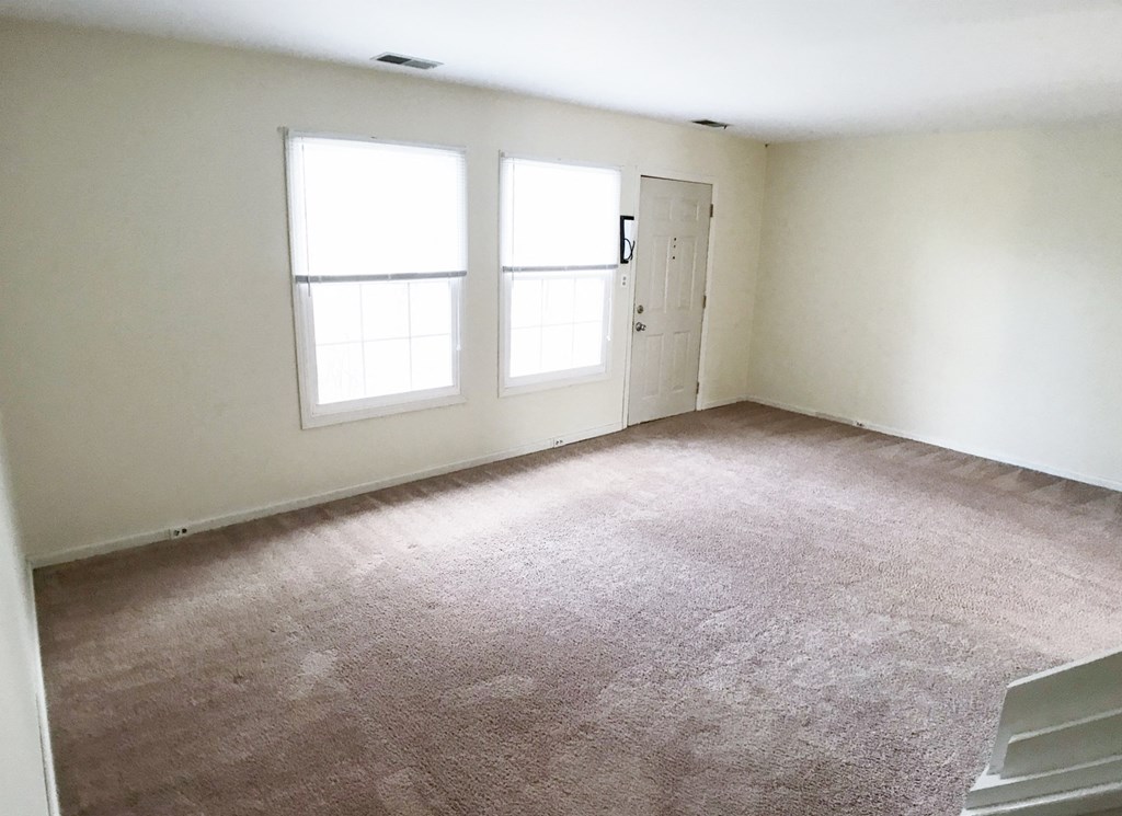 an empty room with a carpeted floor and two windows