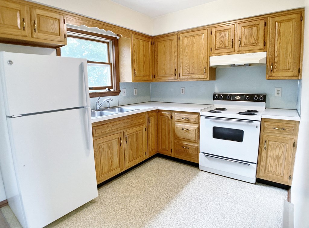 an empty kitchen with white appliances and wooden cabinets