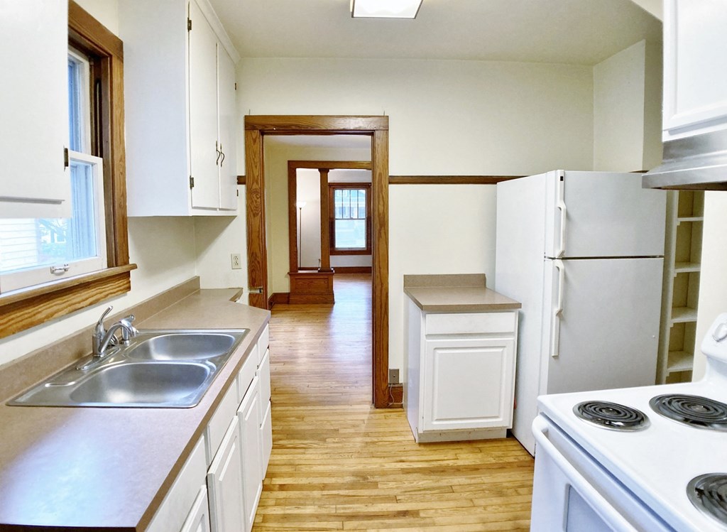 an empty kitchen with white appliances and wooden floors