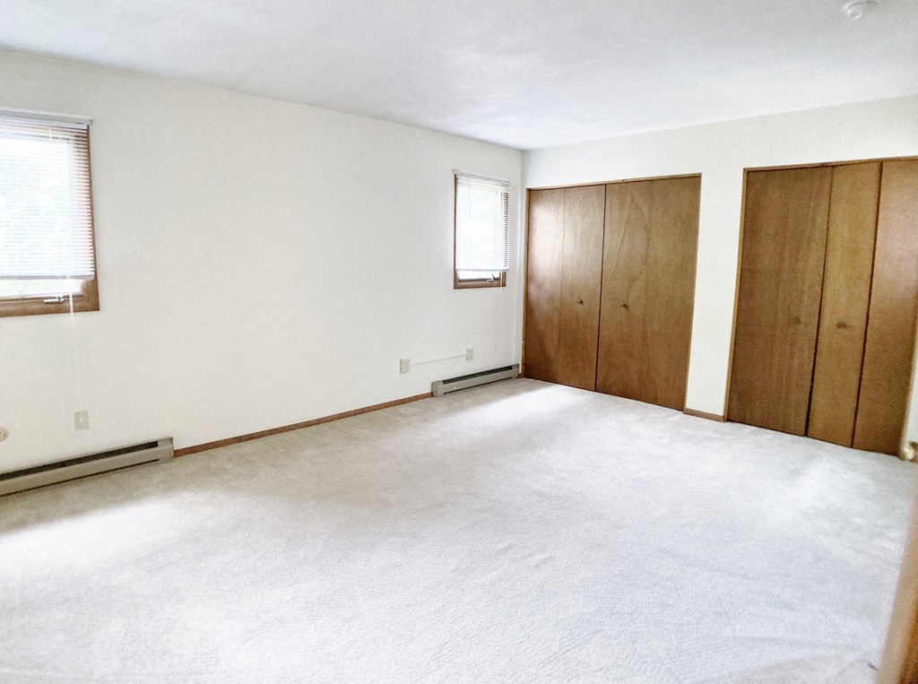 an empty living room with white carpet and wood cabinets