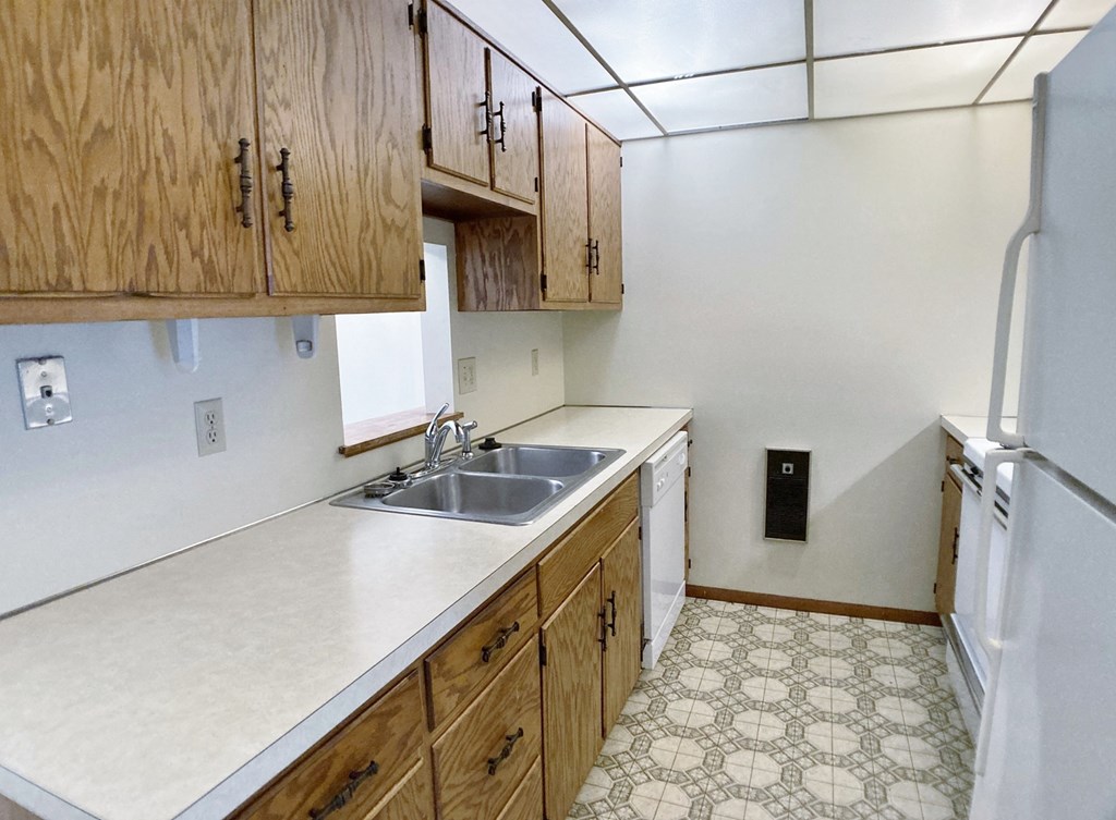 an empty kitchen with white countertops and wooden cabinets