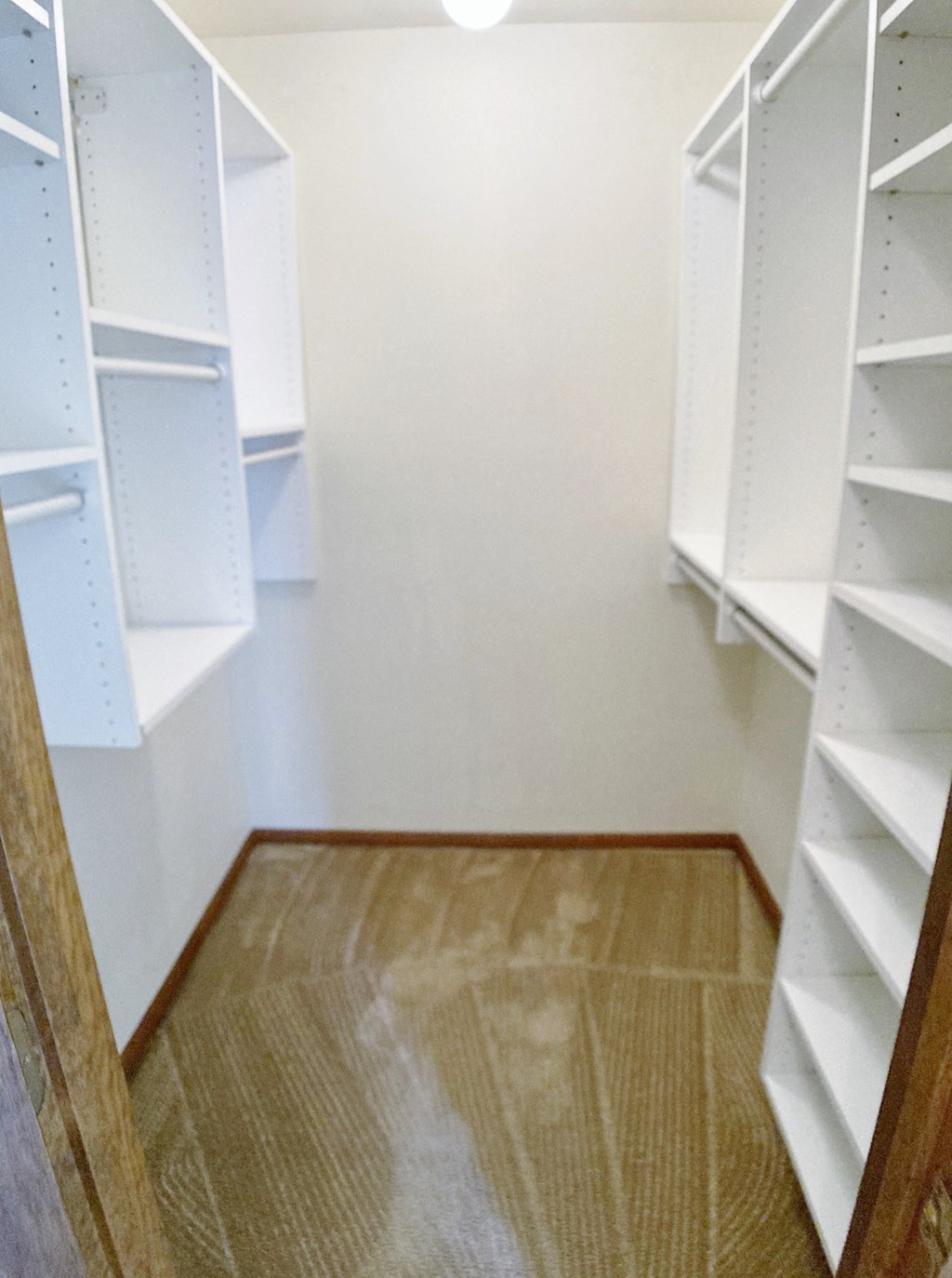a walk in closet with white shelves and wood floors