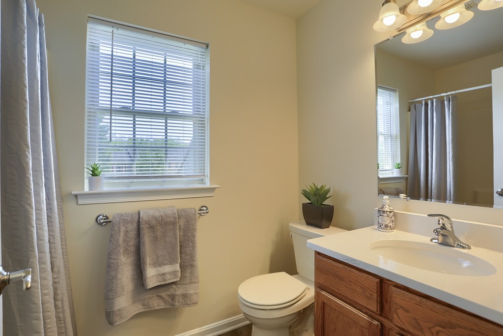 A bathroom with a toilet, sink, and a window with a towel hanging on the wall.