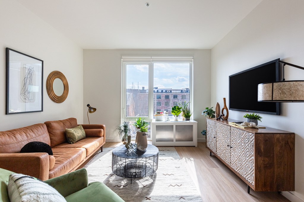 A living room with a brown leather couch, a glass coffee table, and a flat-screen TV mounted on the wall.
