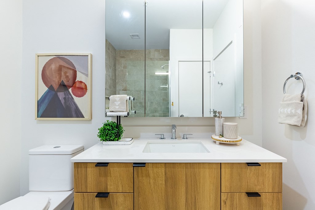A bathroom with a white counter top and a brown cabinet.