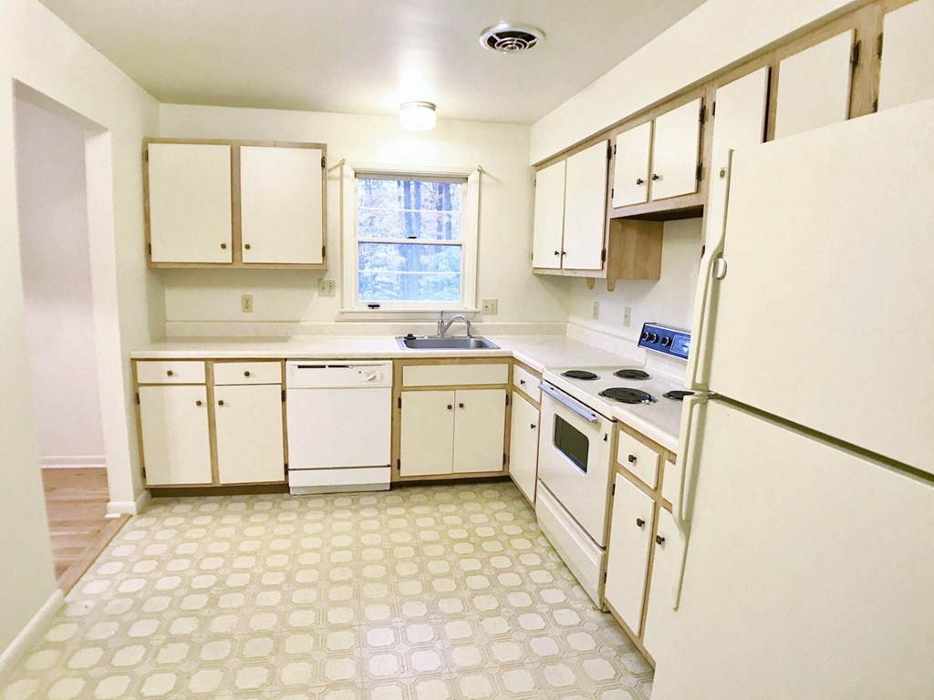 an empty kitchen with white appliances and white cabinets