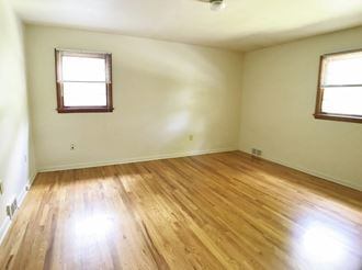 an empty living room with wooden floors and two windows