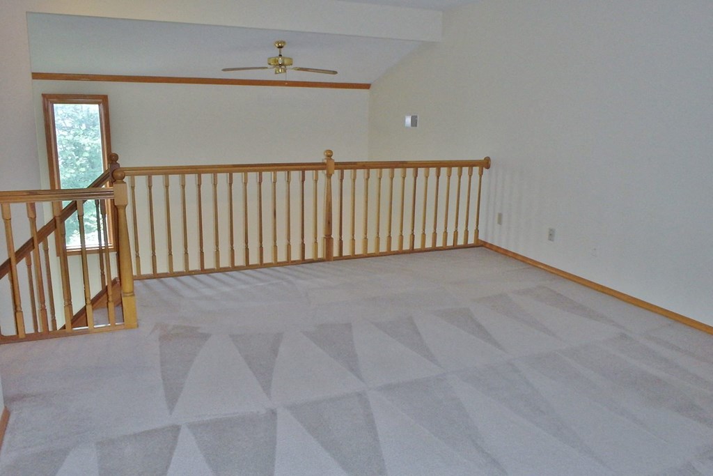 a loft with a landing with a railing and a ceiling fan