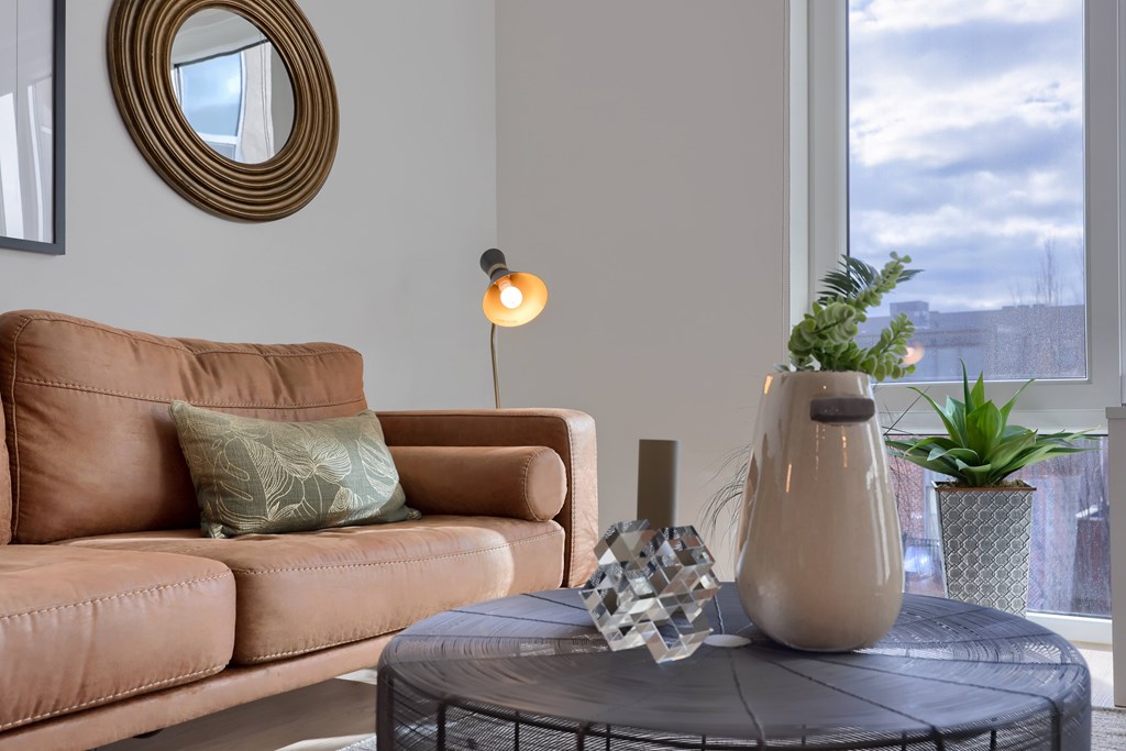 A brown couch with a green pillow and a lamp on a table.