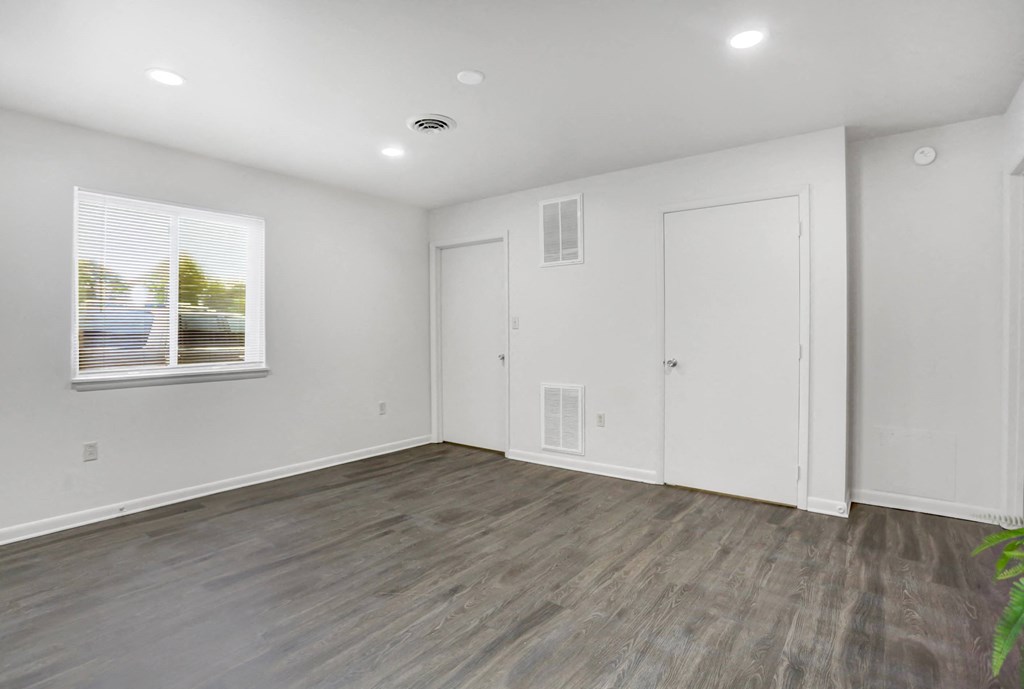 a living room with white walls and wood floors and a window