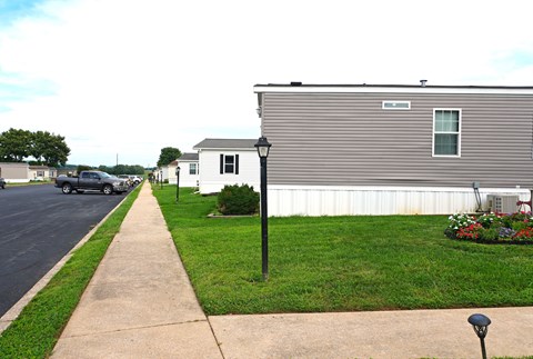 A grey house with a white fence and a green bush in front.