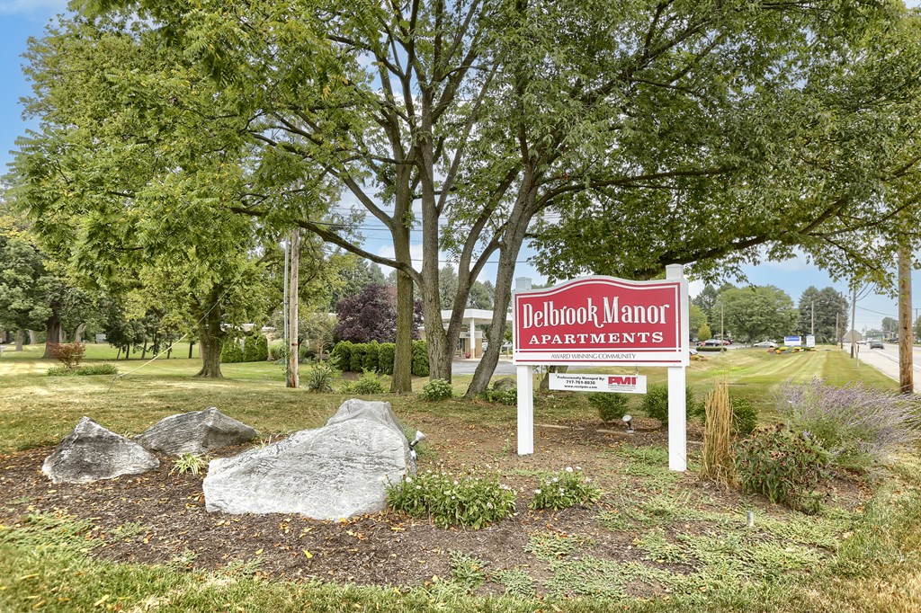 Mechanicsburg Apartments | Delbrook Manor Apartments | a sign in front of a grassy area with trees in the background
