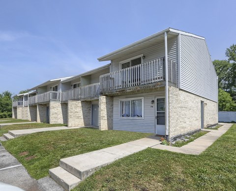 an exterior view of a white and gray apartment building with a sidewalk and grass