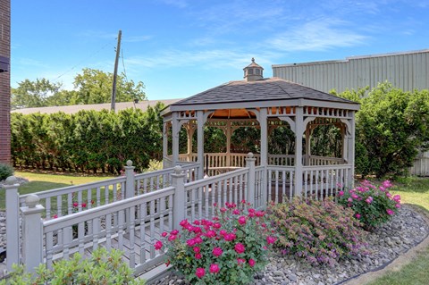 A gazebo surrounded by a white picket fence and pink flowers.