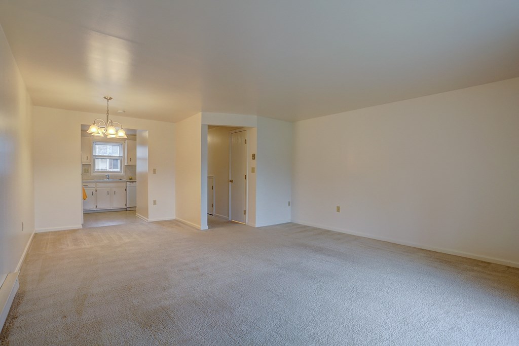 an empty living room with a kitchen in the background