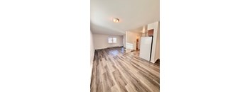 A room with wooden flooring and a white refrigerator.