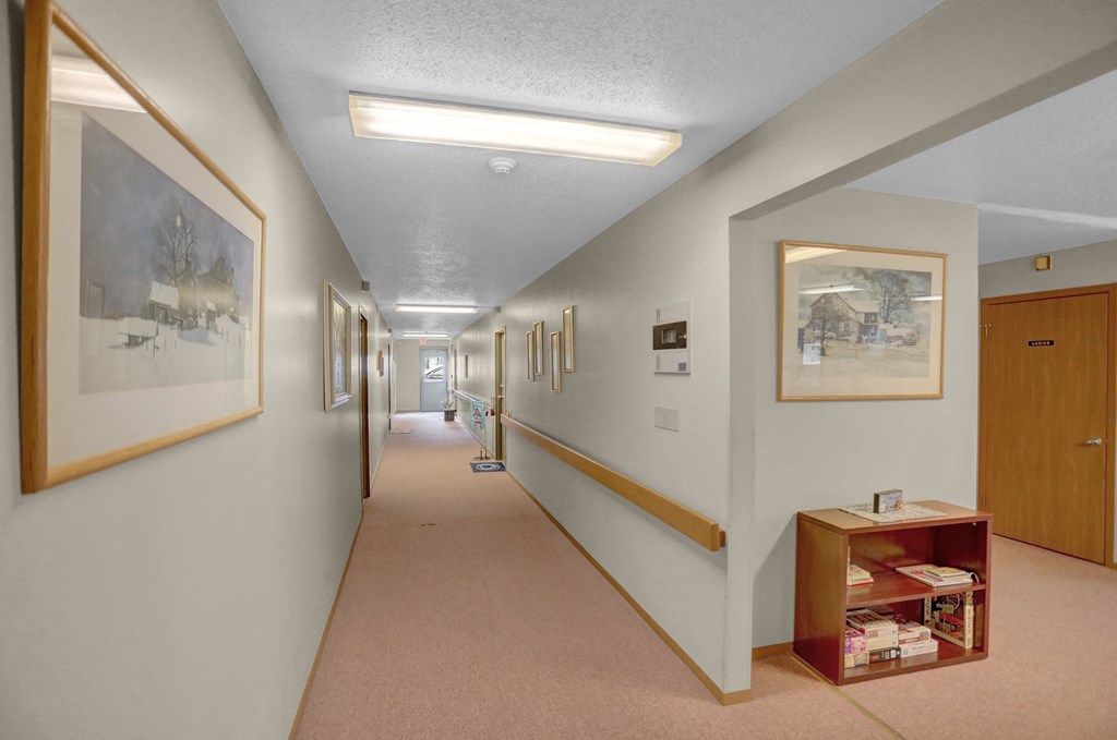 a long corridor with paintings on the walls and a small shelf with books