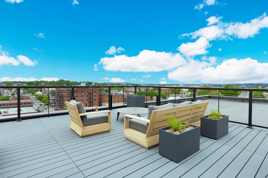 A wooden chair and a sofa are on a wooden deck with a city view.
