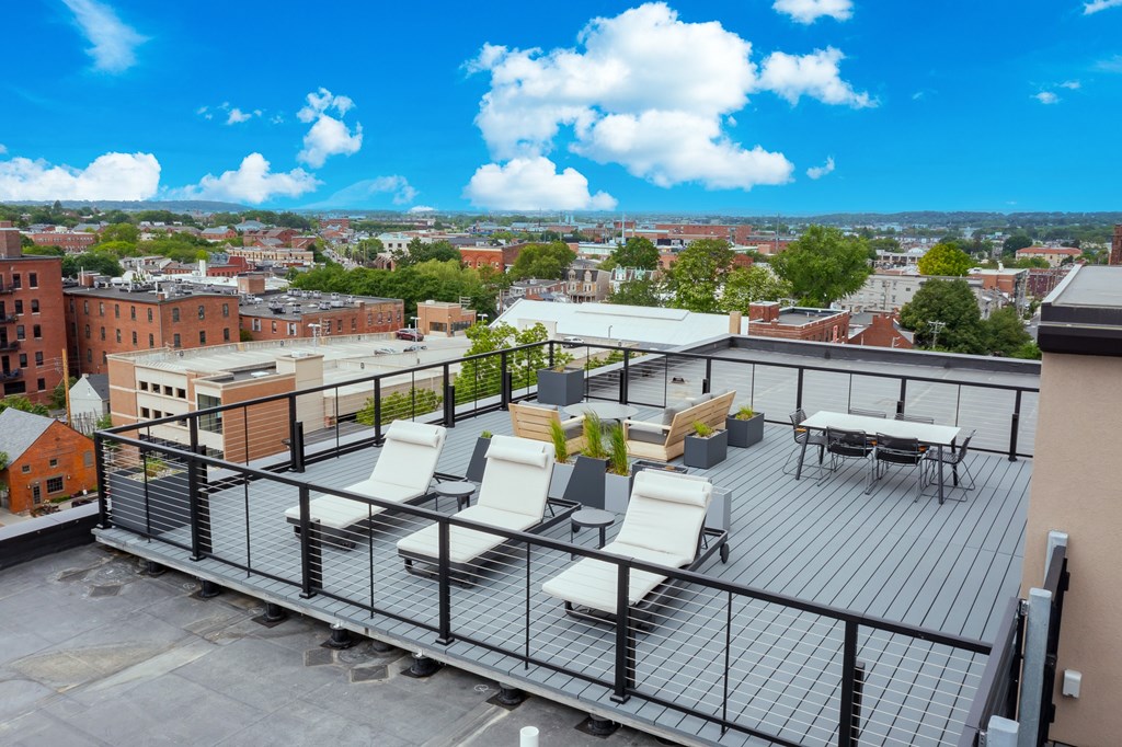 A rooftop patio with white chairs and a table.