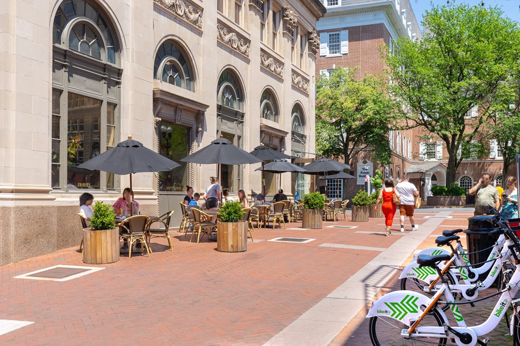 a city street with people sitting at tables and umbrellas