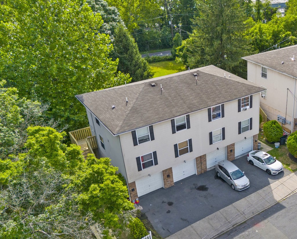 A white two-story house with a brown roof and a parking area in front.