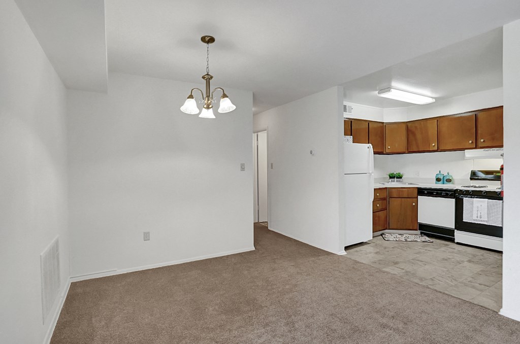 an empty living room with a kitchen with a refrigerator and a sink