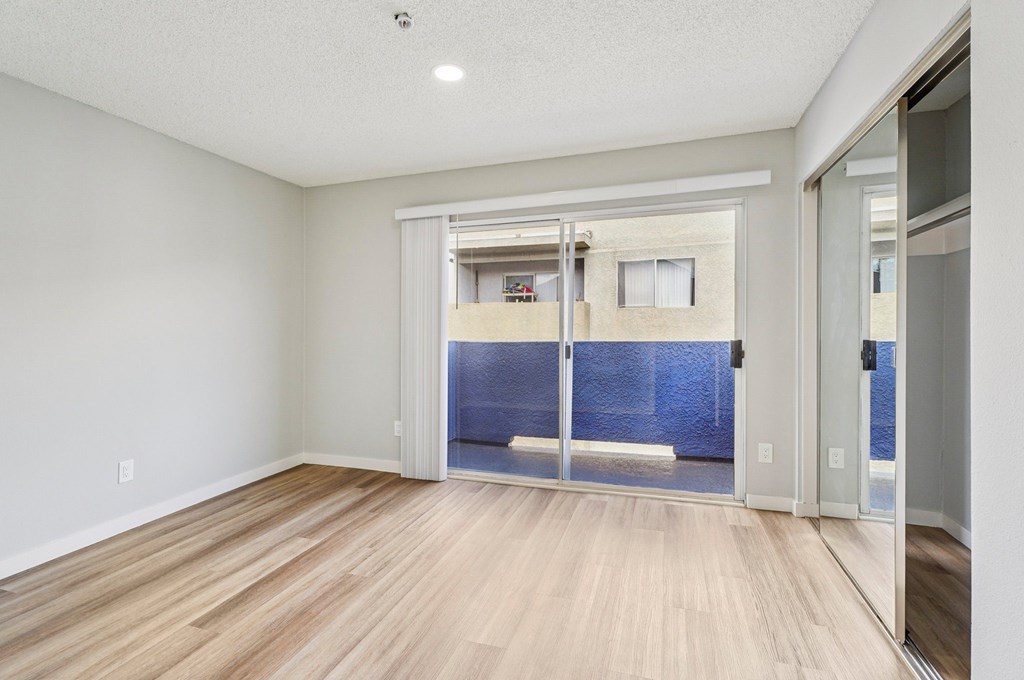 A room with a wooden floor and a glass door leading to a balcony.