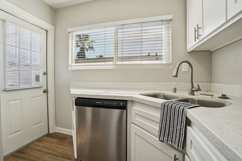 A kitchen with a stainless steel dishwasher and a window with blinds.