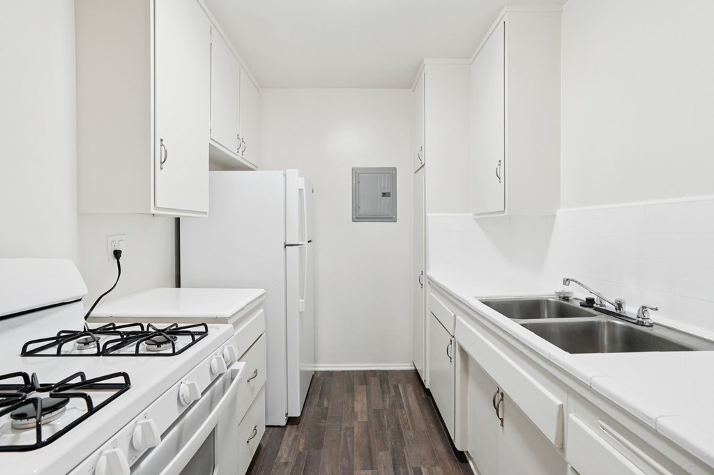 A white kitchen with a stove, sink, and refrigerator.