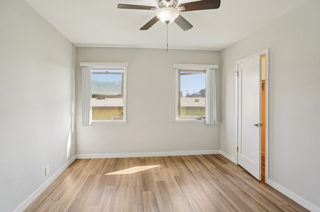 A room with a ceiling fan and two windows.
