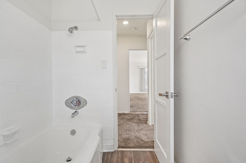A white bathroom with a tub and a doorway leading to another room.