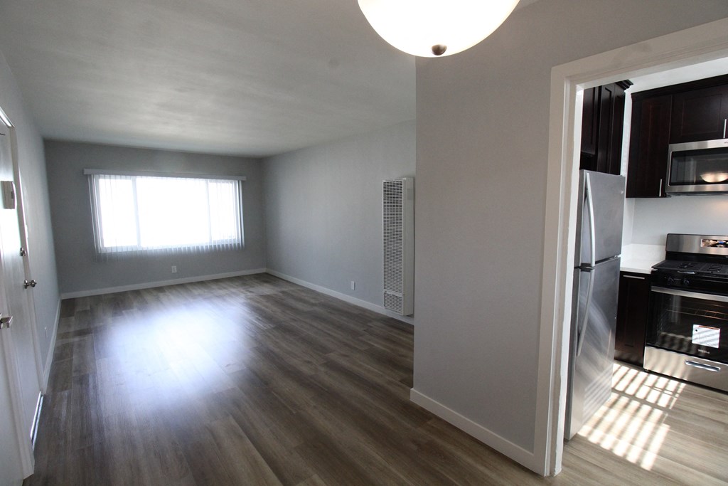 an empty living room with a kitchen in the background
