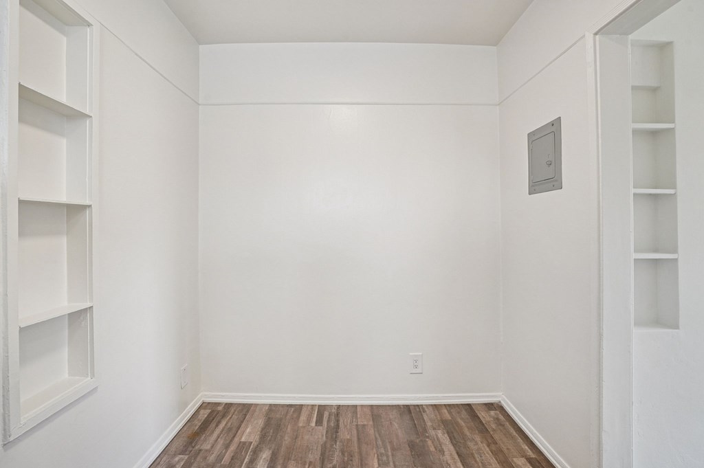 A white room with wood flooring and built-in shelves.