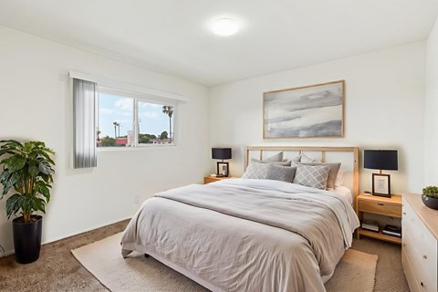 A bedroom with a large bed, a potted plant, and a painting on the wall.