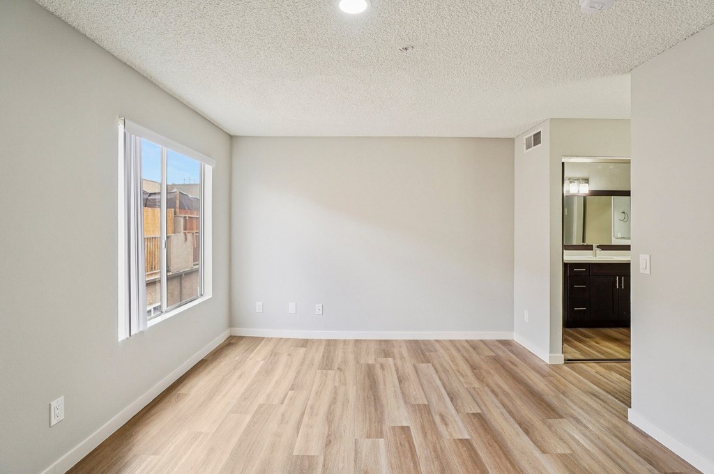 A room with wooden flooring and a window overlooking a building.
