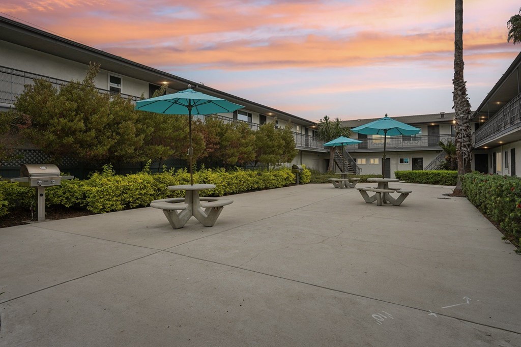 A courtyard with tables and umbrellas surrounded by buildings.