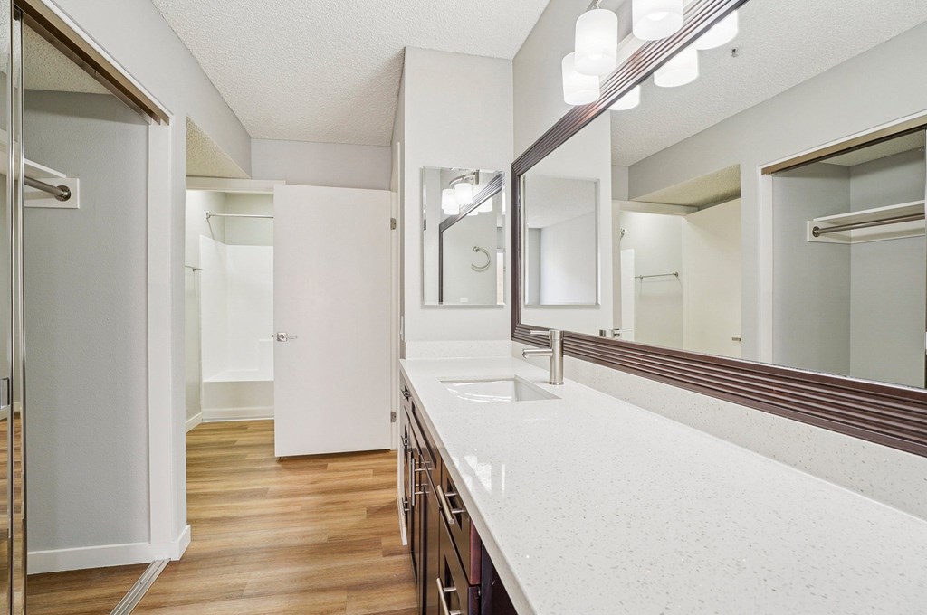 A bathroom with a white counter top and a mirror.