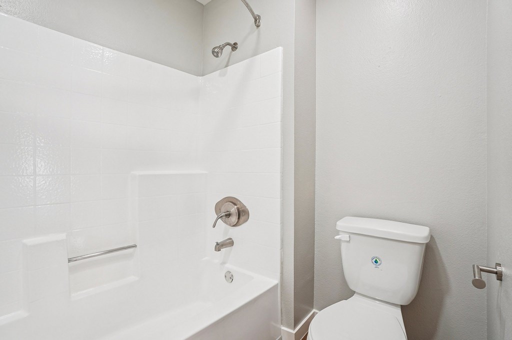 A white toilet with a blue logo on the lid sits next to a white bathtub.