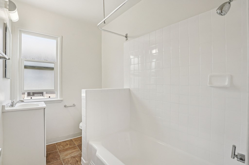 A white bathroom with a tub, sink, and window.