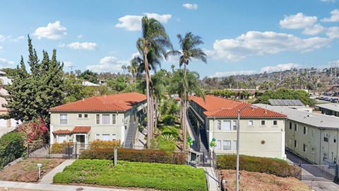 A house with a red roof is surrounded by greenery and other houses.