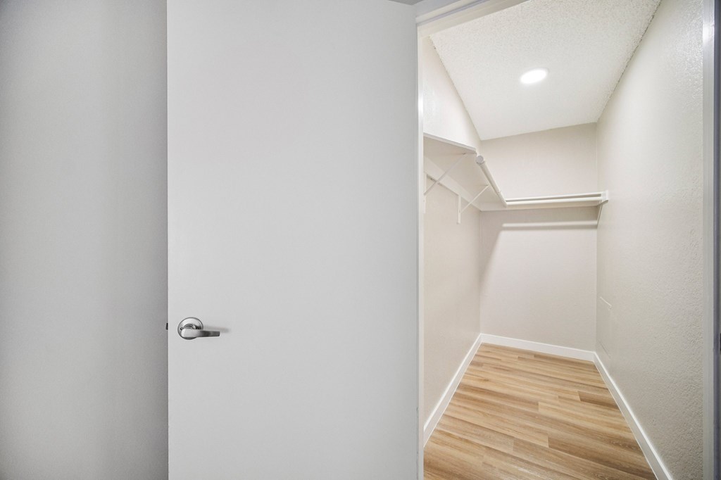 A white door with a silver handle is open to a hallway with wooden floors.