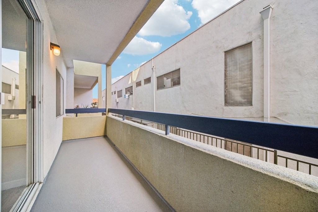 A long, narrow balcony with a black railing and a white wall.