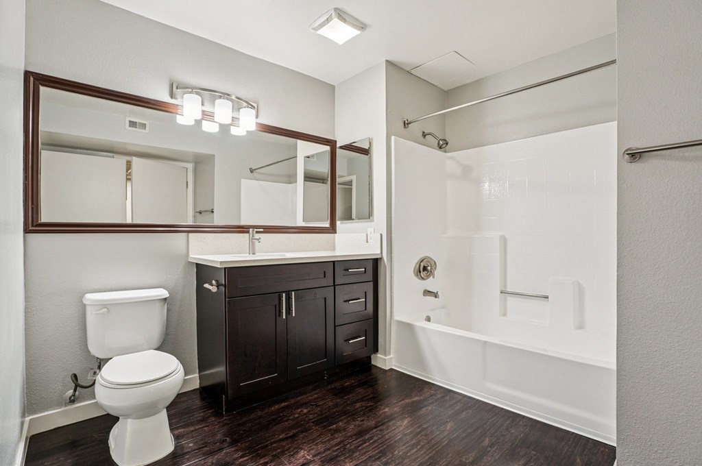 A white toilet sits in a bathroom with a wooden floor and a large mirror above it.