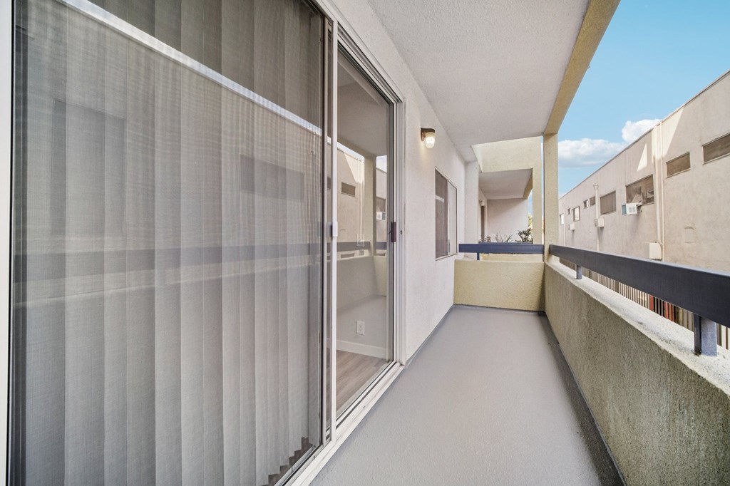 A long, narrow balcony with a glass door and a concrete wall.