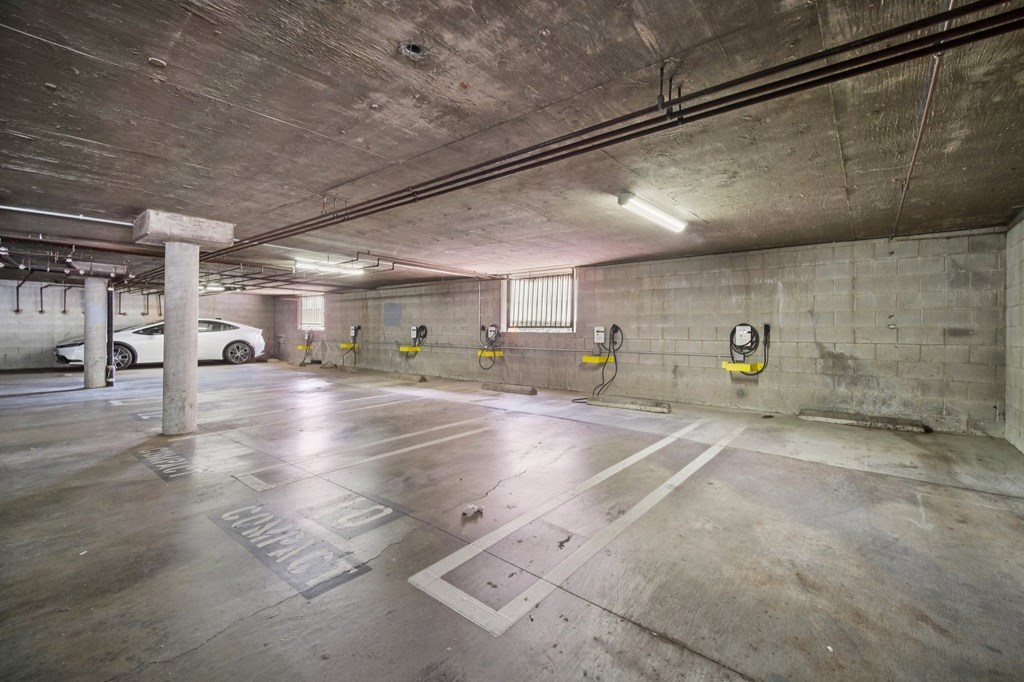 A parking garage with concrete walls and floor, and a few cars parked.