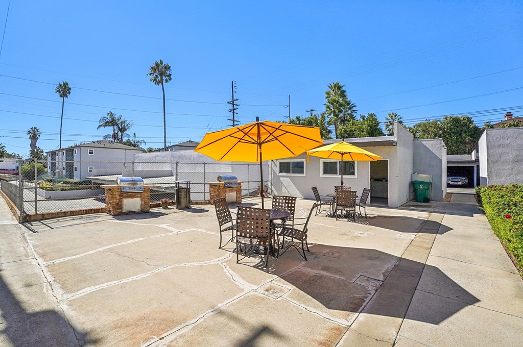 A patio with a yellow umbrella and chairs.