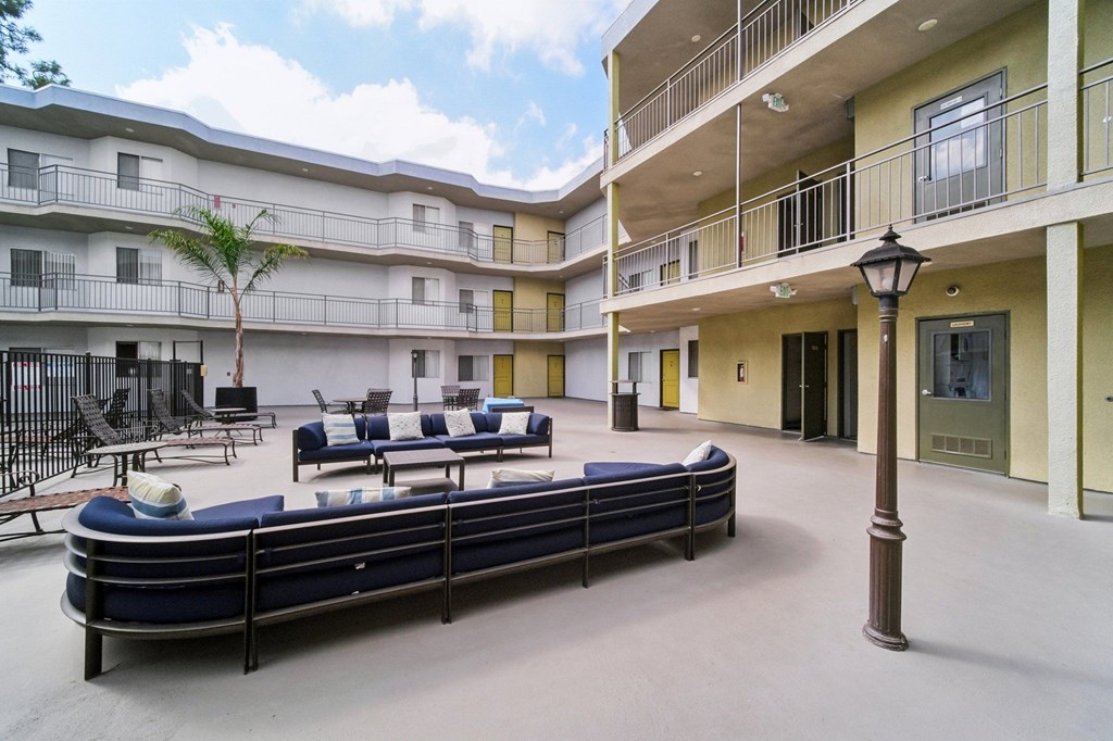 A patio area with a long black bench and a tree in front of apartment buildings.